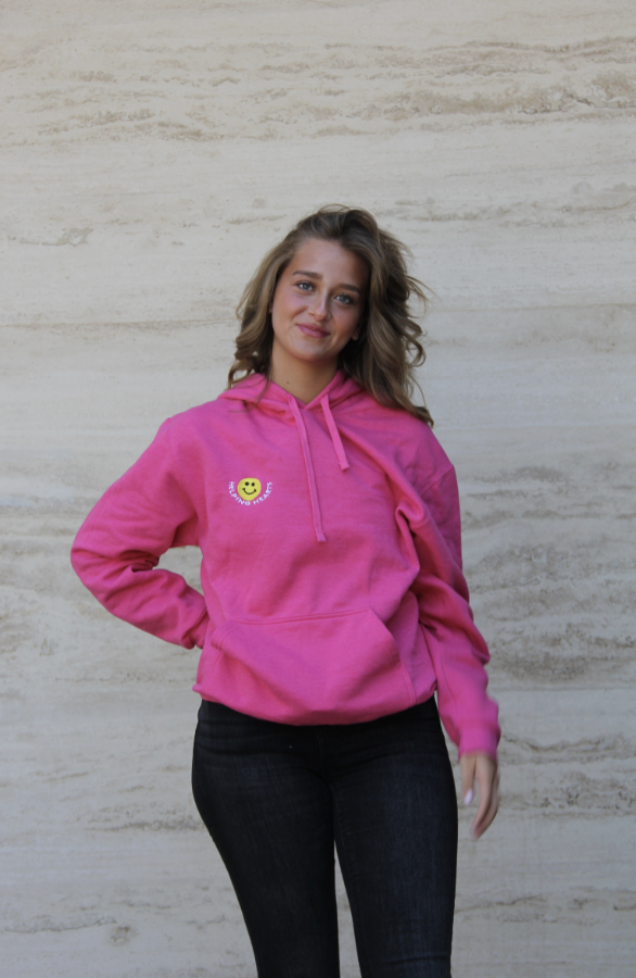 Hoodie rosa vivo — vista frontal con carita feliz y logo Helping Hearts